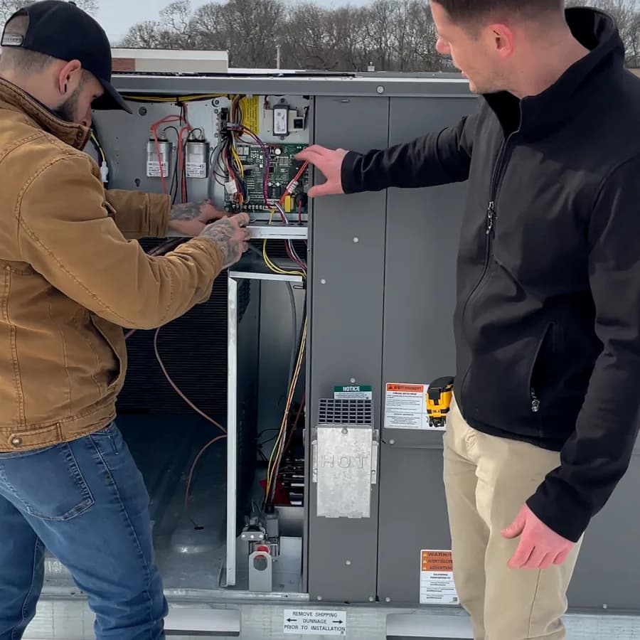 Two Kintech technicians wiring the controls of a rooftop unit