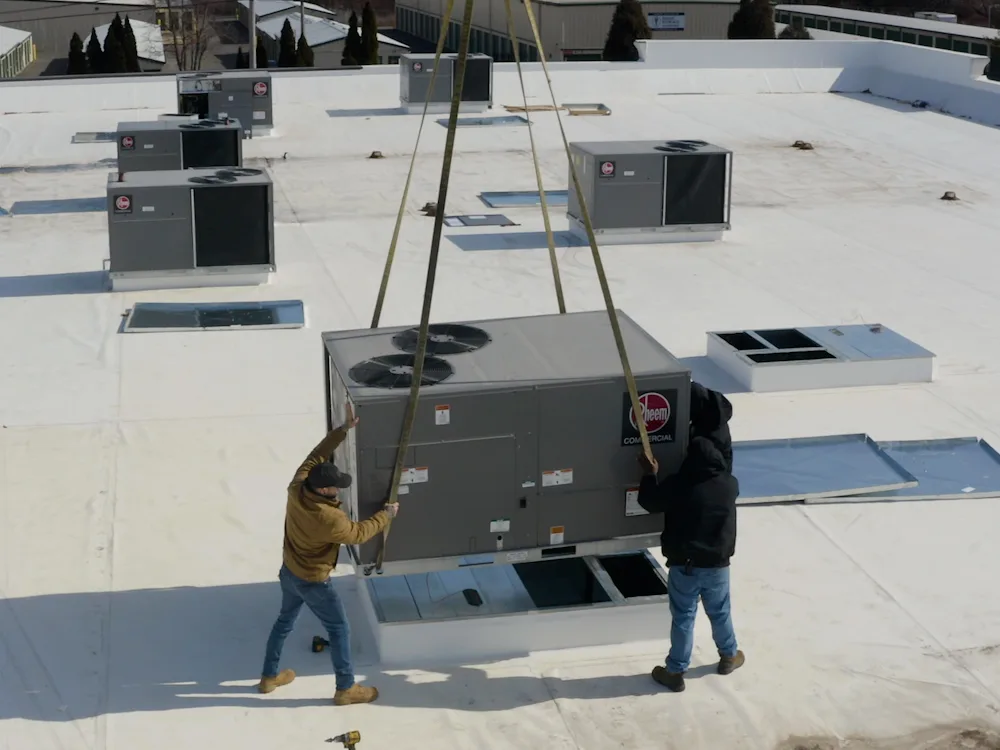A Kintech crew guiding a new rooftop unit down from a crane onto a commercial roof
