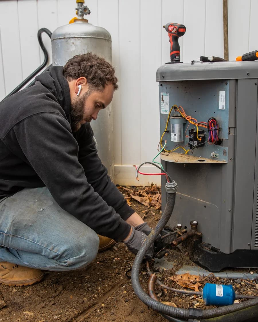 Kintech technician repairing a heat pump outdoor unit with the panel open