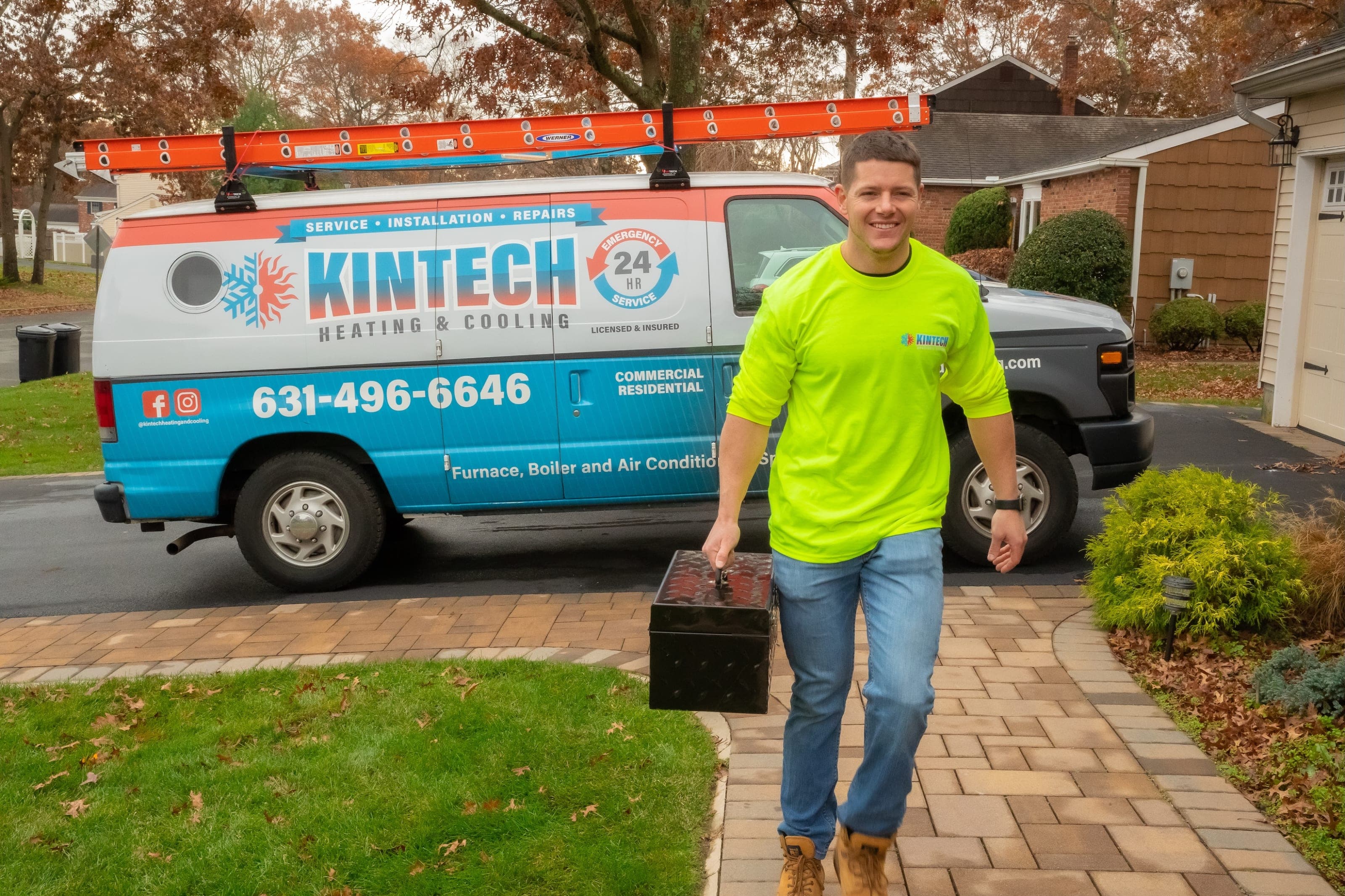 A Kintech technician carrying a toolbox up a driveway, the Kintech van parked behind him