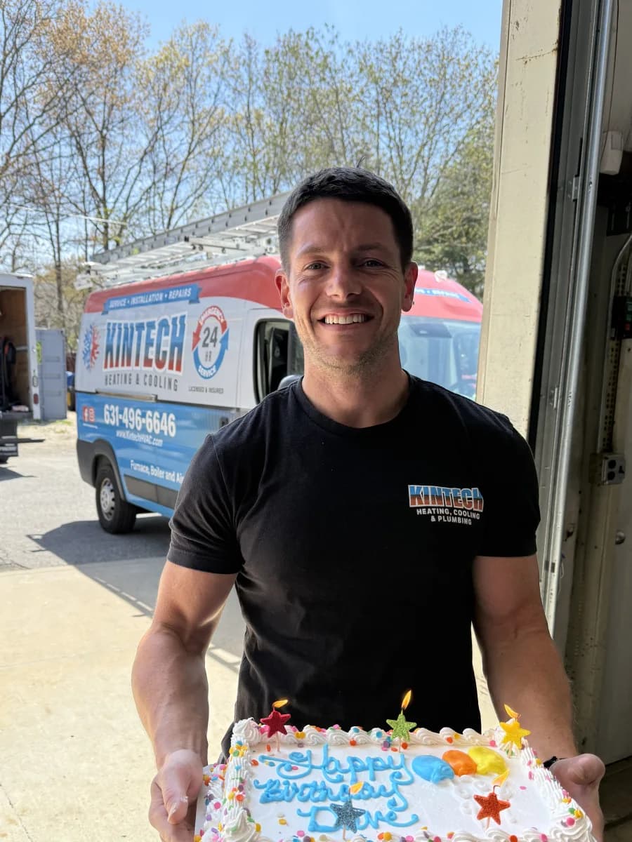 A Kintech team member grinning with a birthday cake outside the shop, a van behind him
