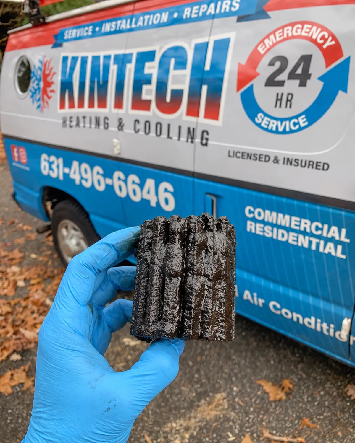 An oil burner's cartridge filter after one heating season, black with sludge, held up in front of a Kintech van