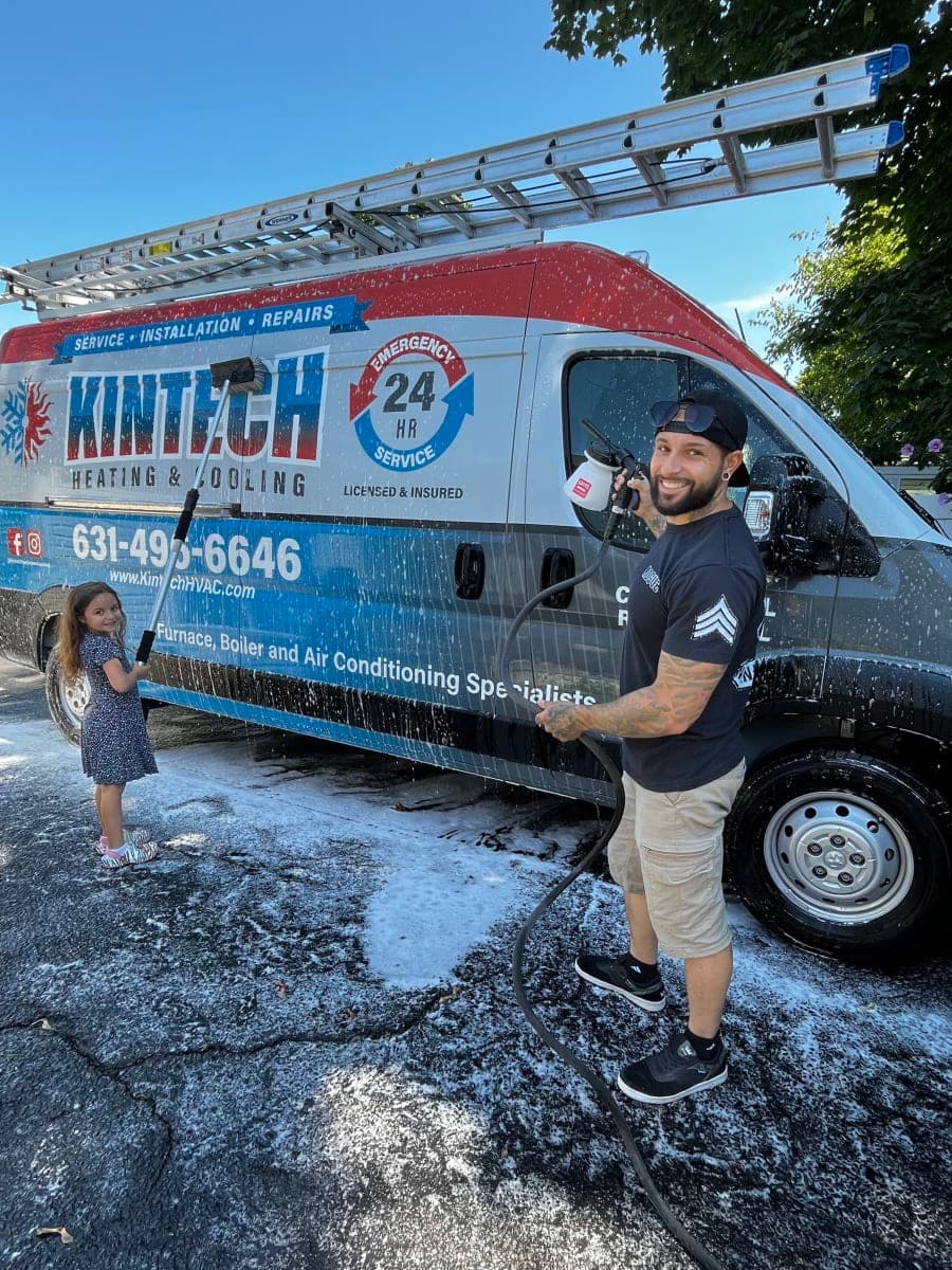 A Kintech technician washing the Kintech van on a sunny day, a young helper scrubbing beside him