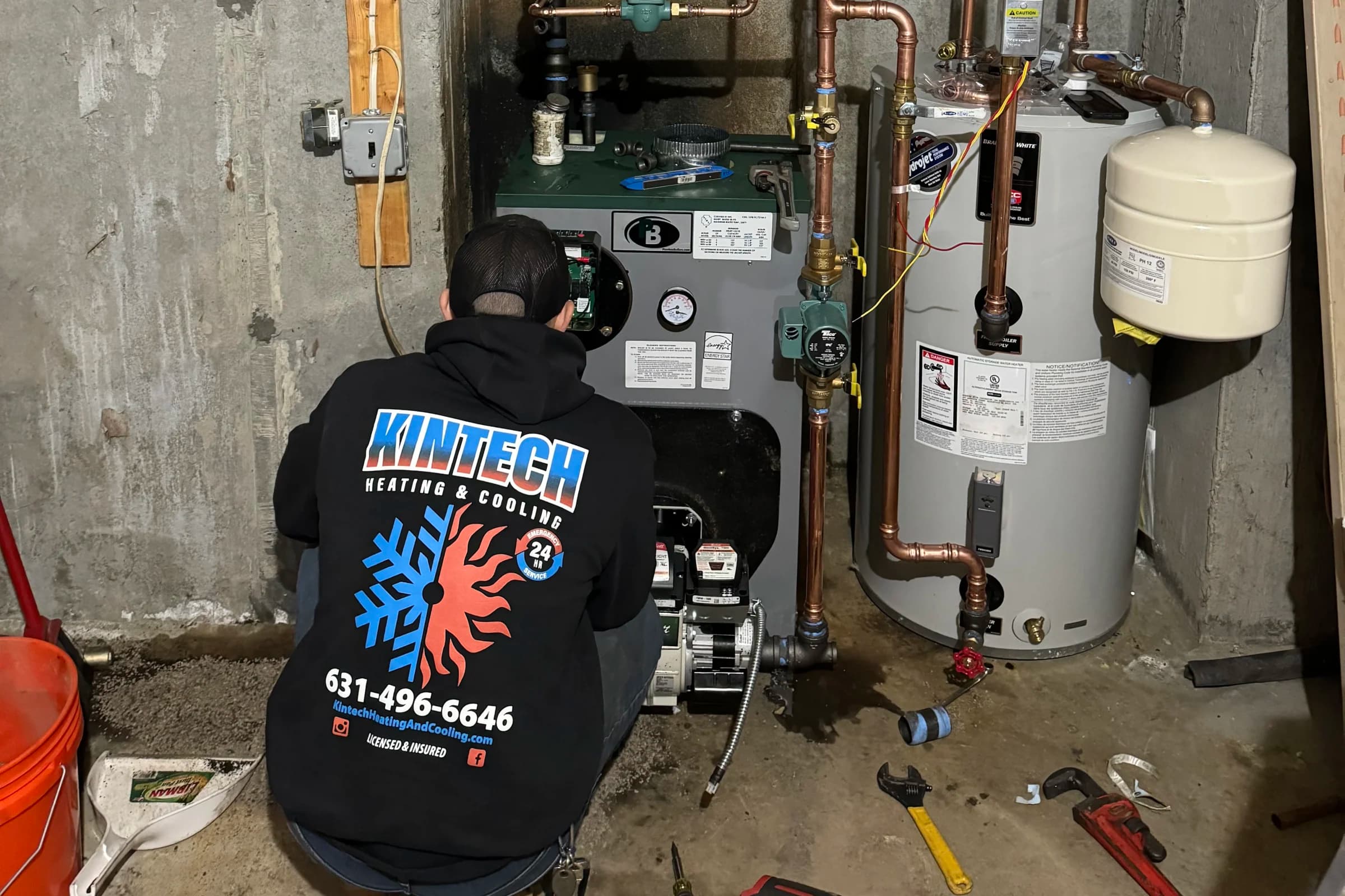 A Kintech technician kneeling at an oil-fired boiler, working on its burner